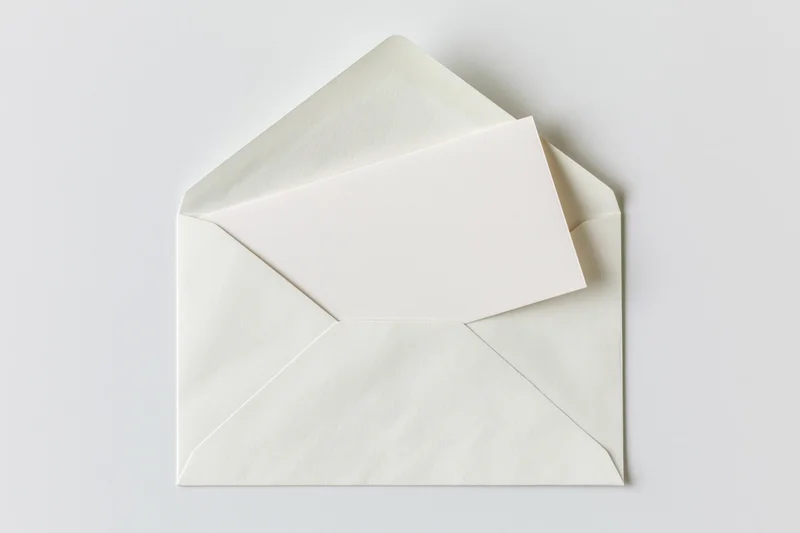 Open white paper envelope with blank card partially pulled out on plain surface