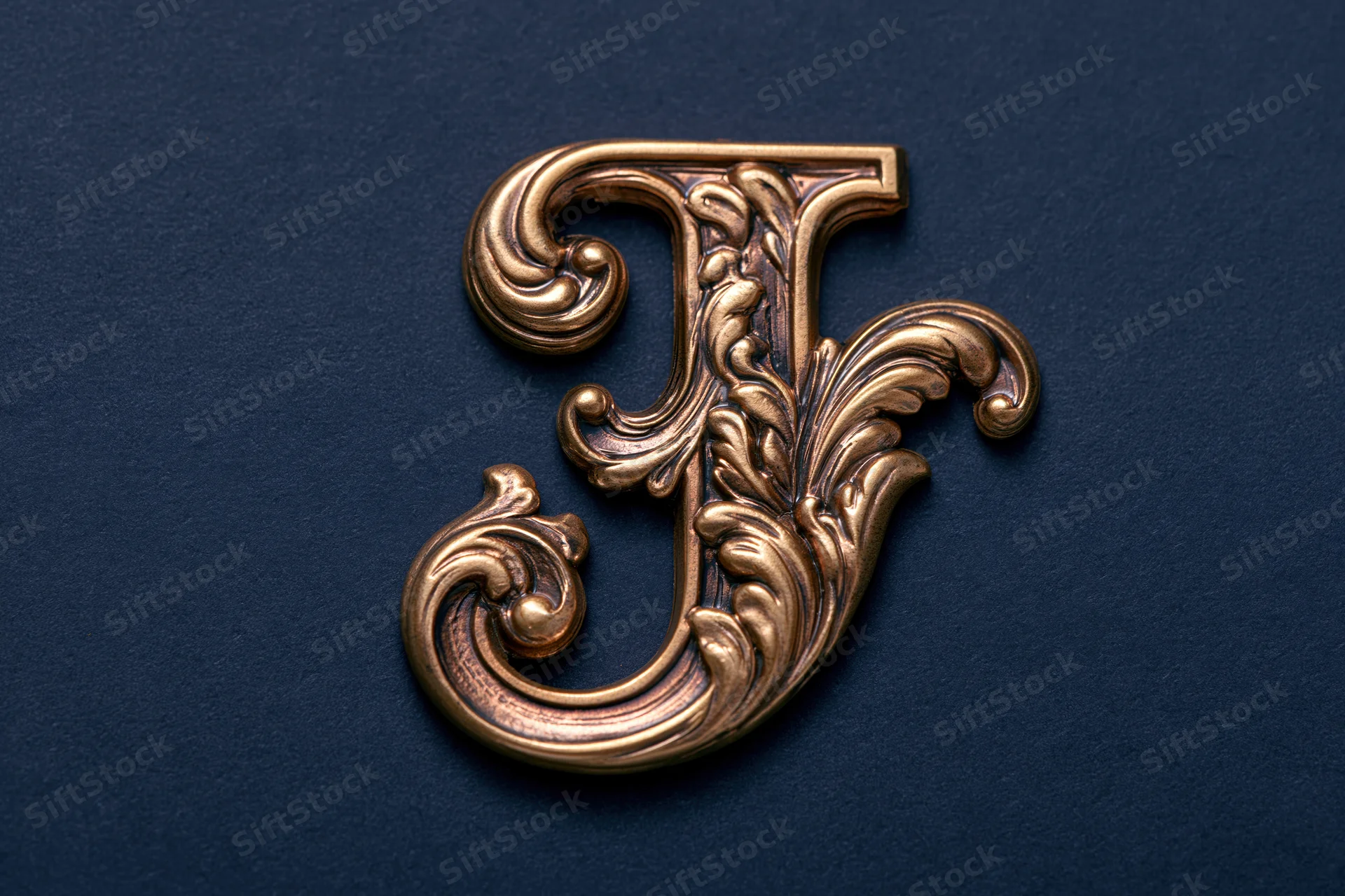 Ornate gold letter j with baroque floral scroll engravings on dark blue background