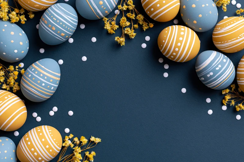 Painted easter eggs in blue and yellow with floral accents arranged in a border on navy background with copyspace