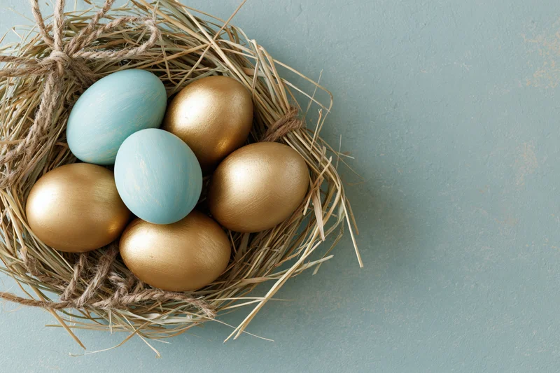 Golden and blue painted easter eggs in a straw nest on a mint surface
