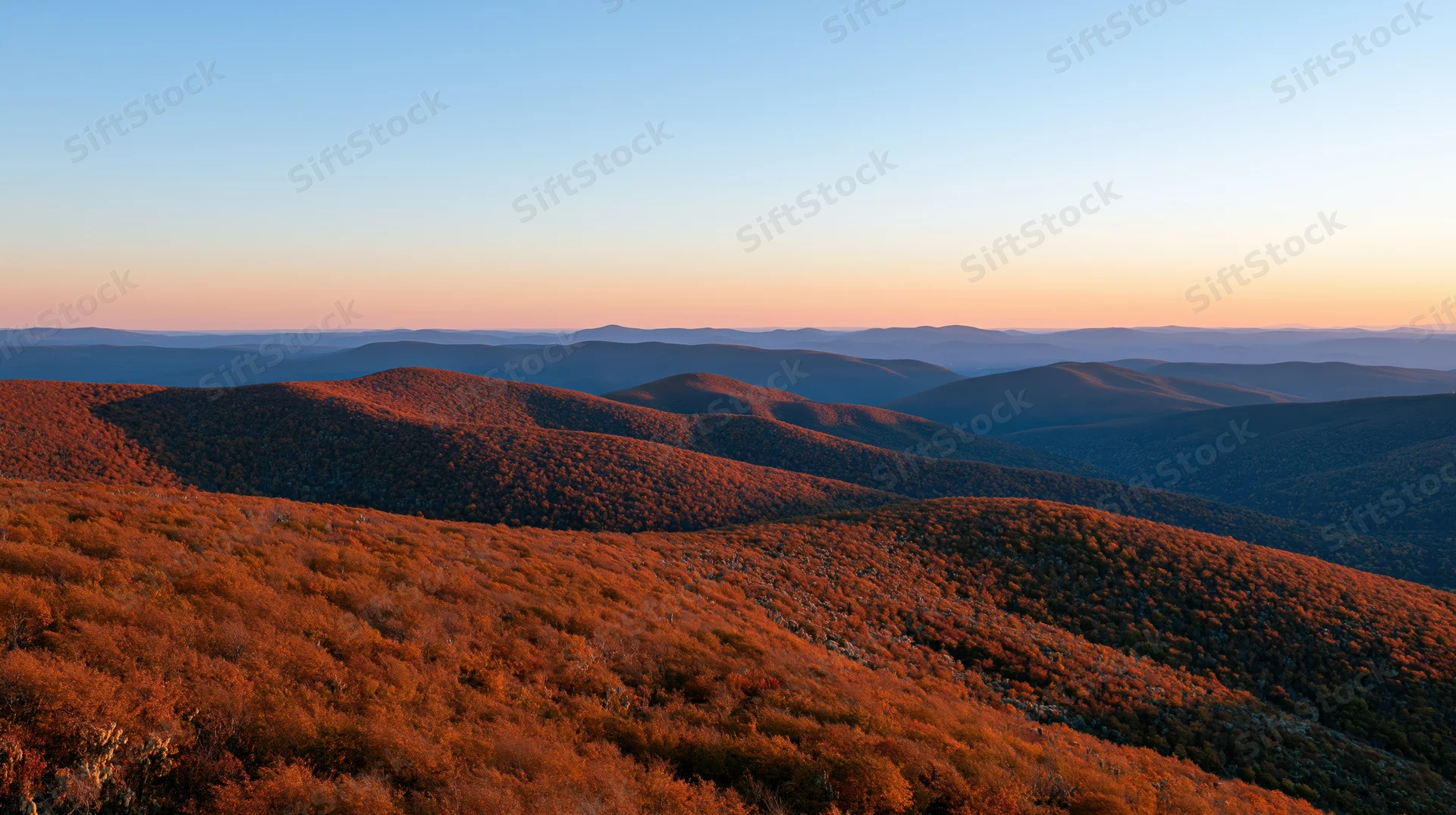 Panoramic view of rolling autumn hills covered in colorful foliage under a twilight sky from a high ridge