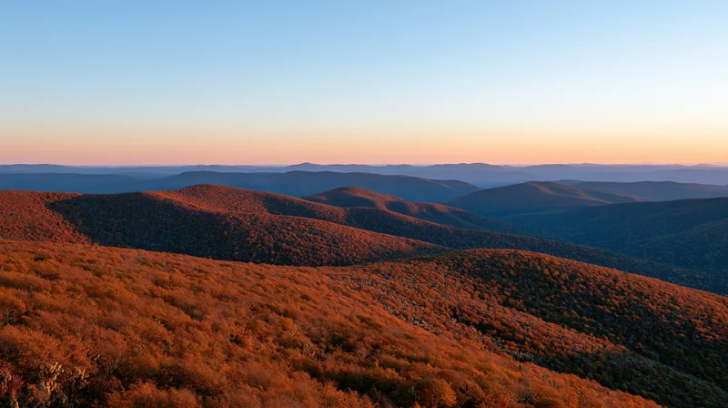 Panoramic view of rolling autumn hills covered in colorful foliage under a twilight sky from a high ridge