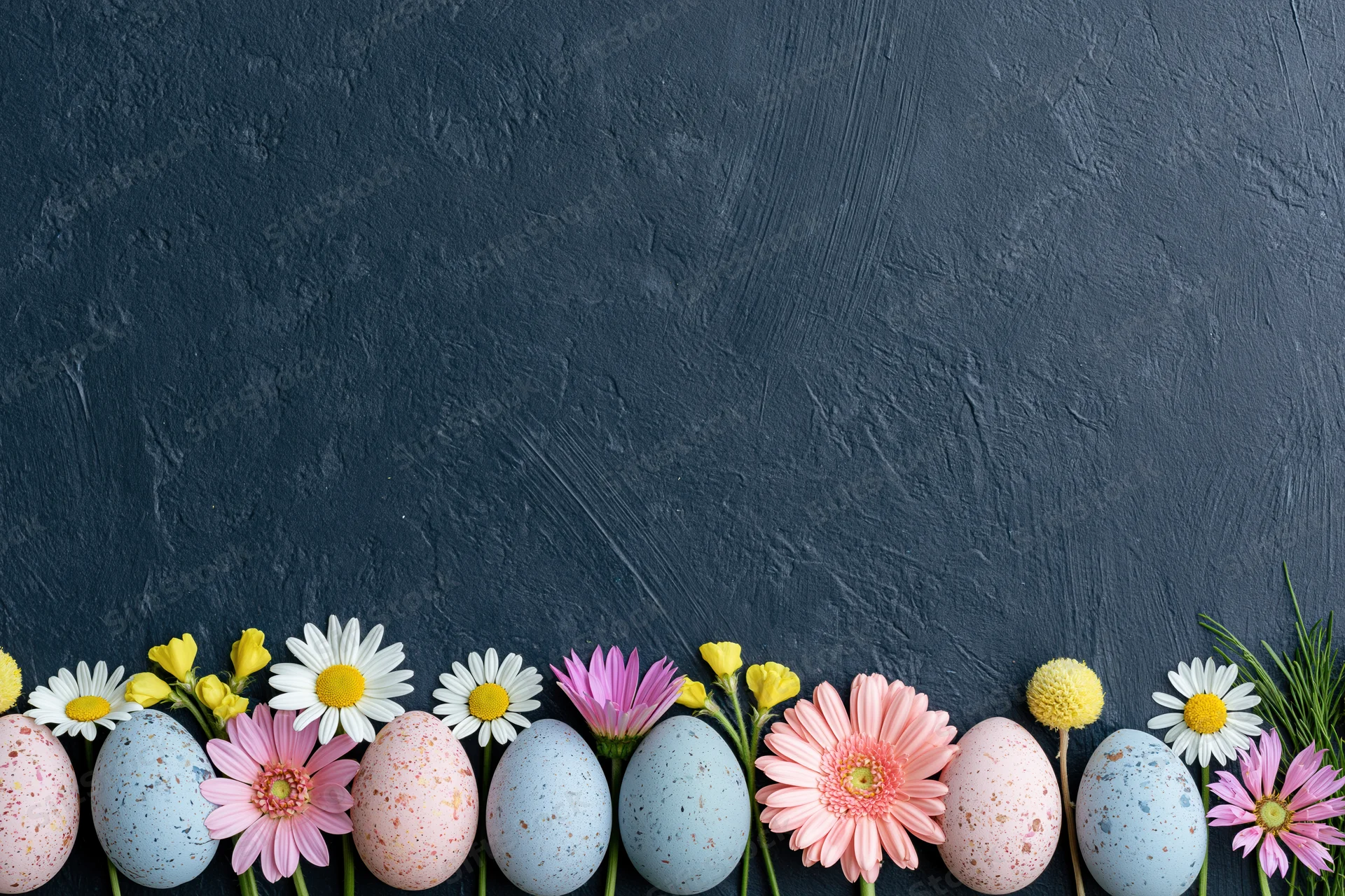 Pastel speckled easter eggs and spring flowers arranged in a row along the bottom of a dark textured surface