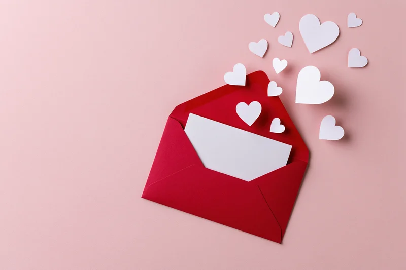 Open red envelope with white paper hearts emerging on pink surface