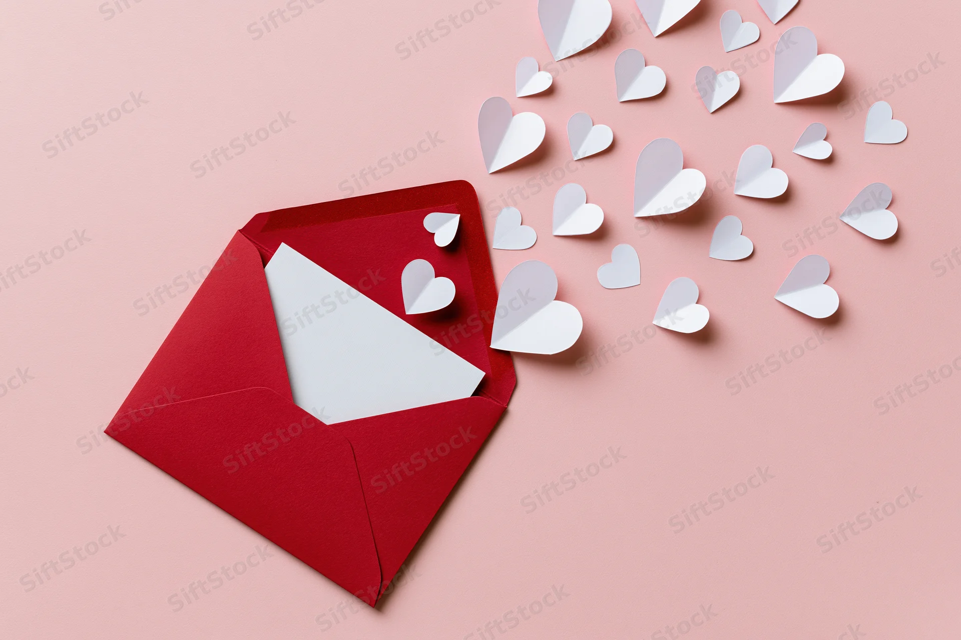 Open red envelope with white paper hearts emerging onto a pink surface