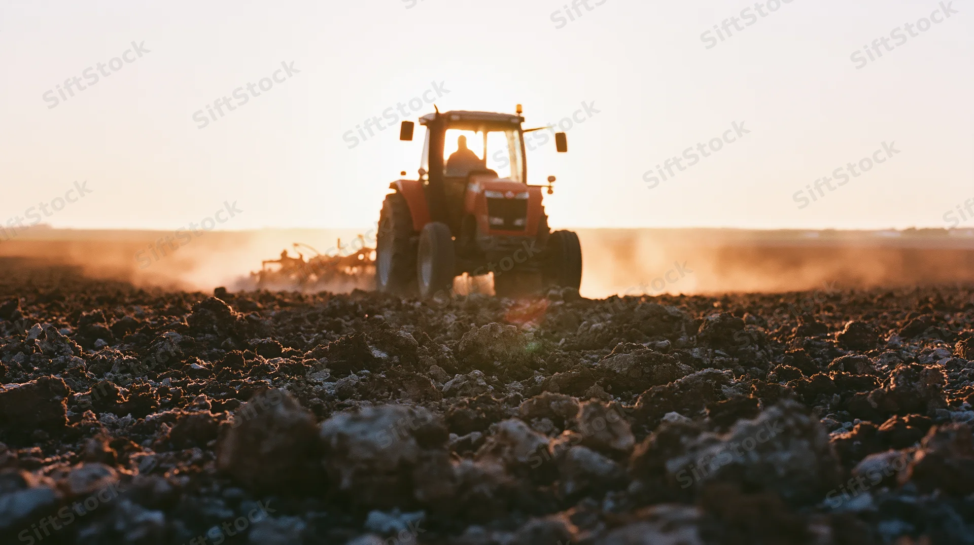 Red tractor pulling tillage implement across freshly tilled field at sunset