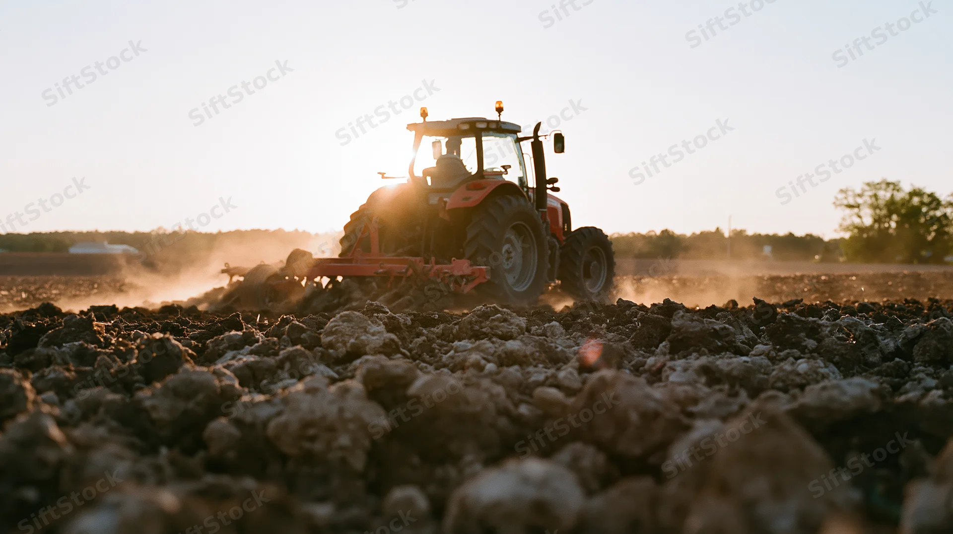 Red tractor pulling tillage implement across freshly tilled field at sunset