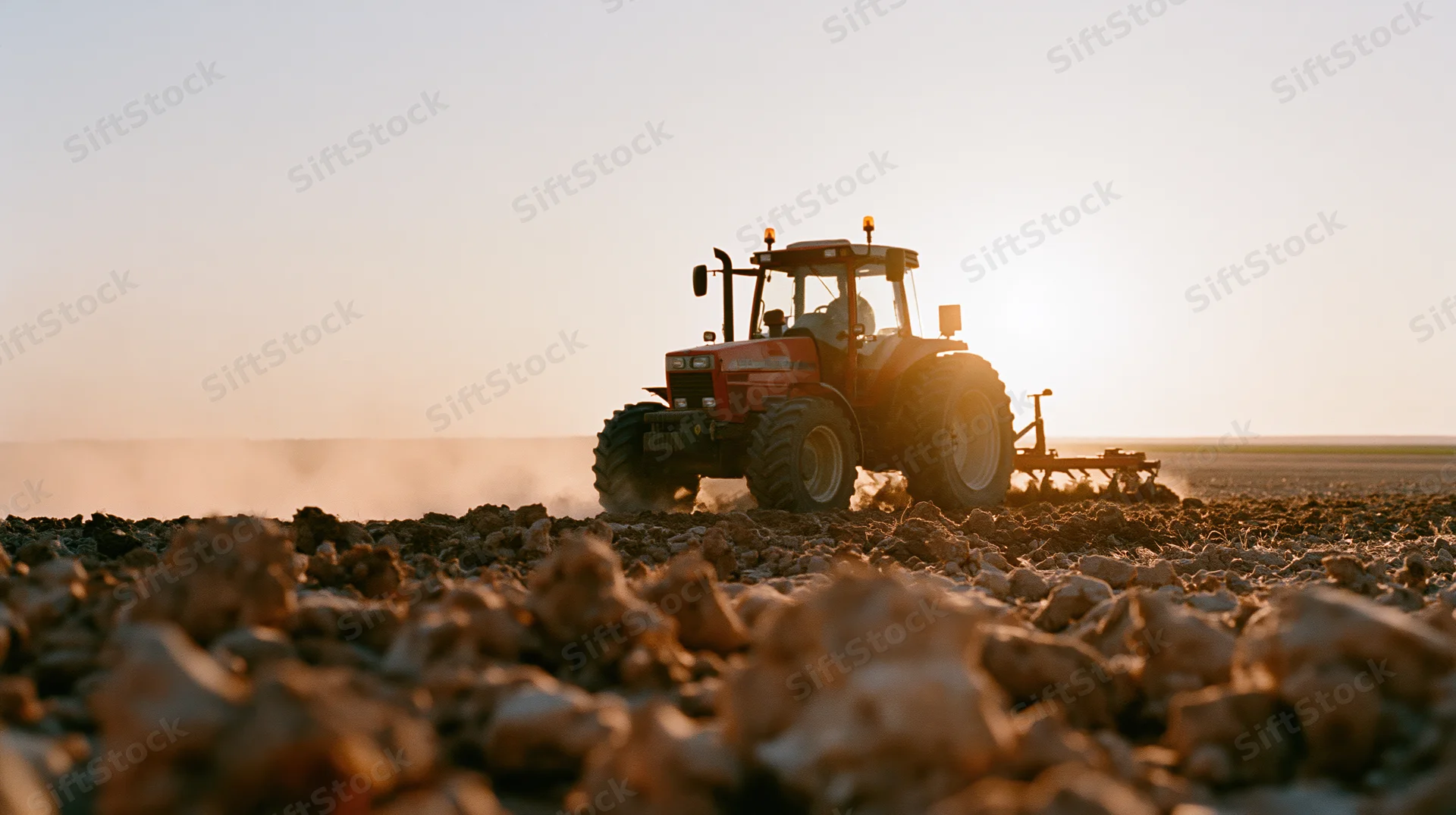 Red tractor pulling tillage implement across freshly tilled field at sunset