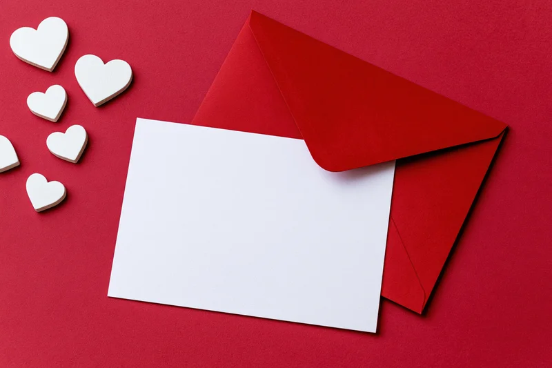 Red envelope with blank white card and wooden hearts on red surface