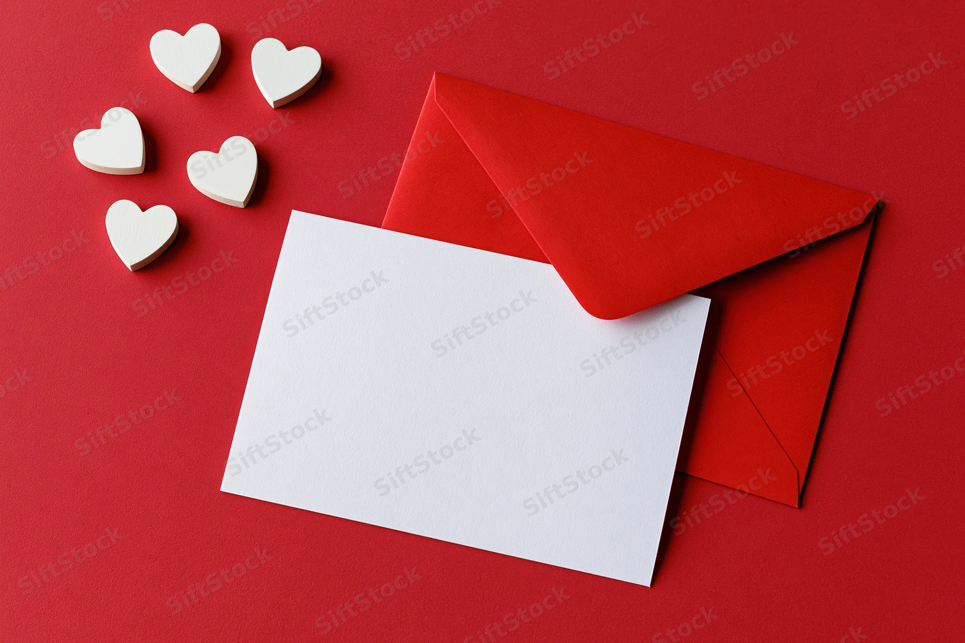 Red envelope with blank white card and wooden hearts on red surface