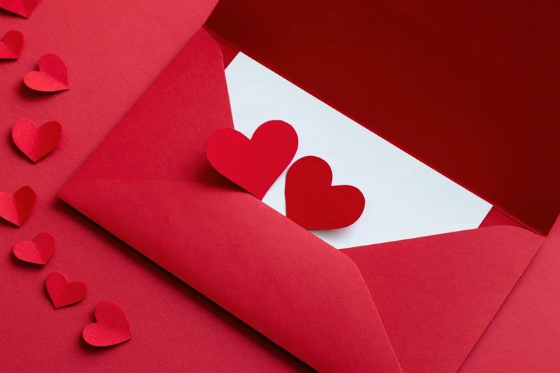 Open red envelope with paper hearts on red surface