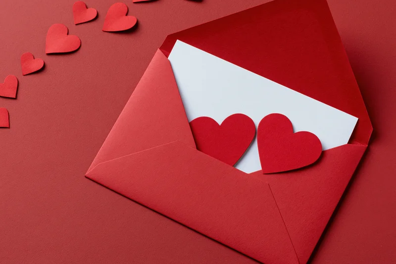 Open red envelope with paper hearts and white card on red surface