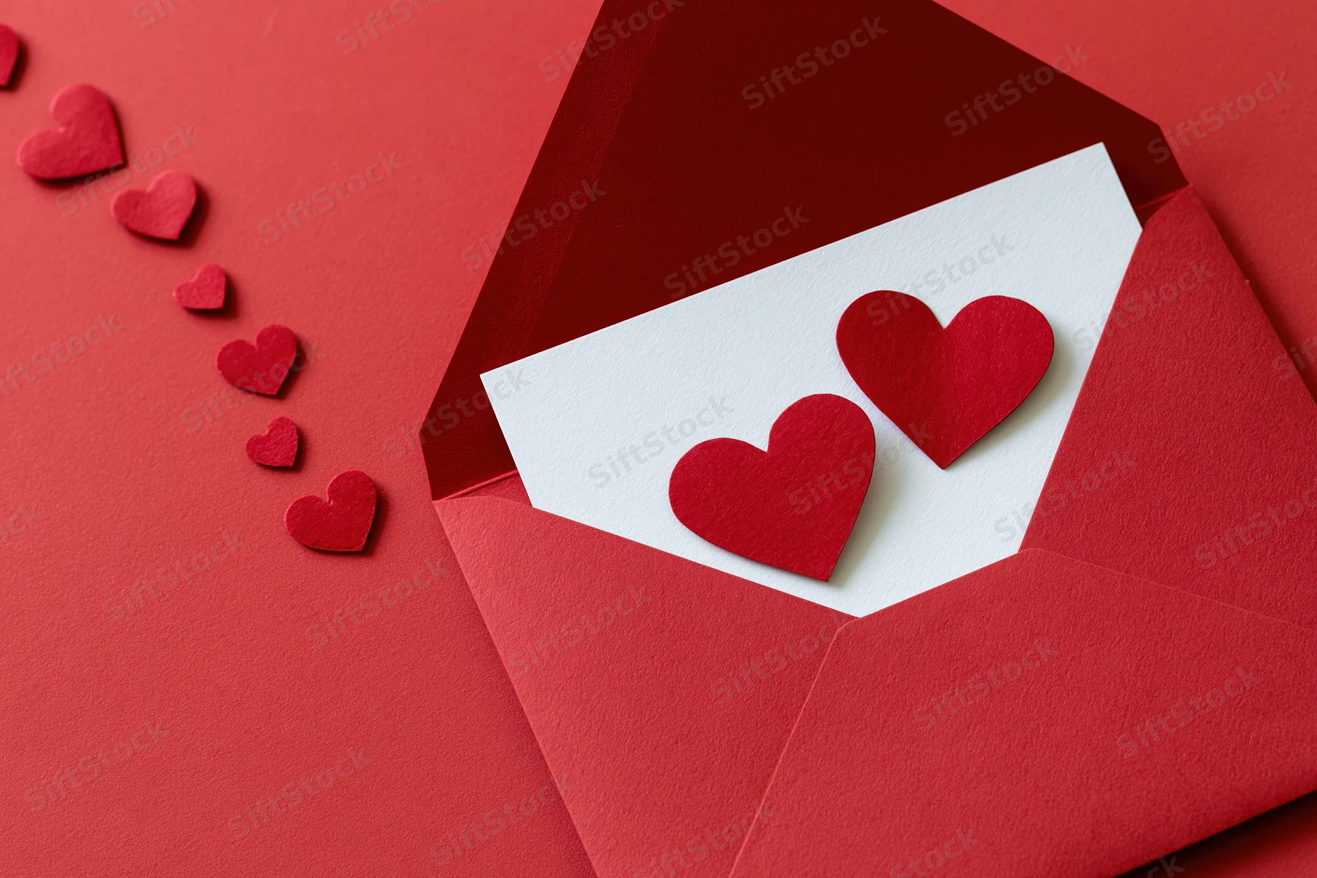 Open red envelope with two red hearts on white card on red surface