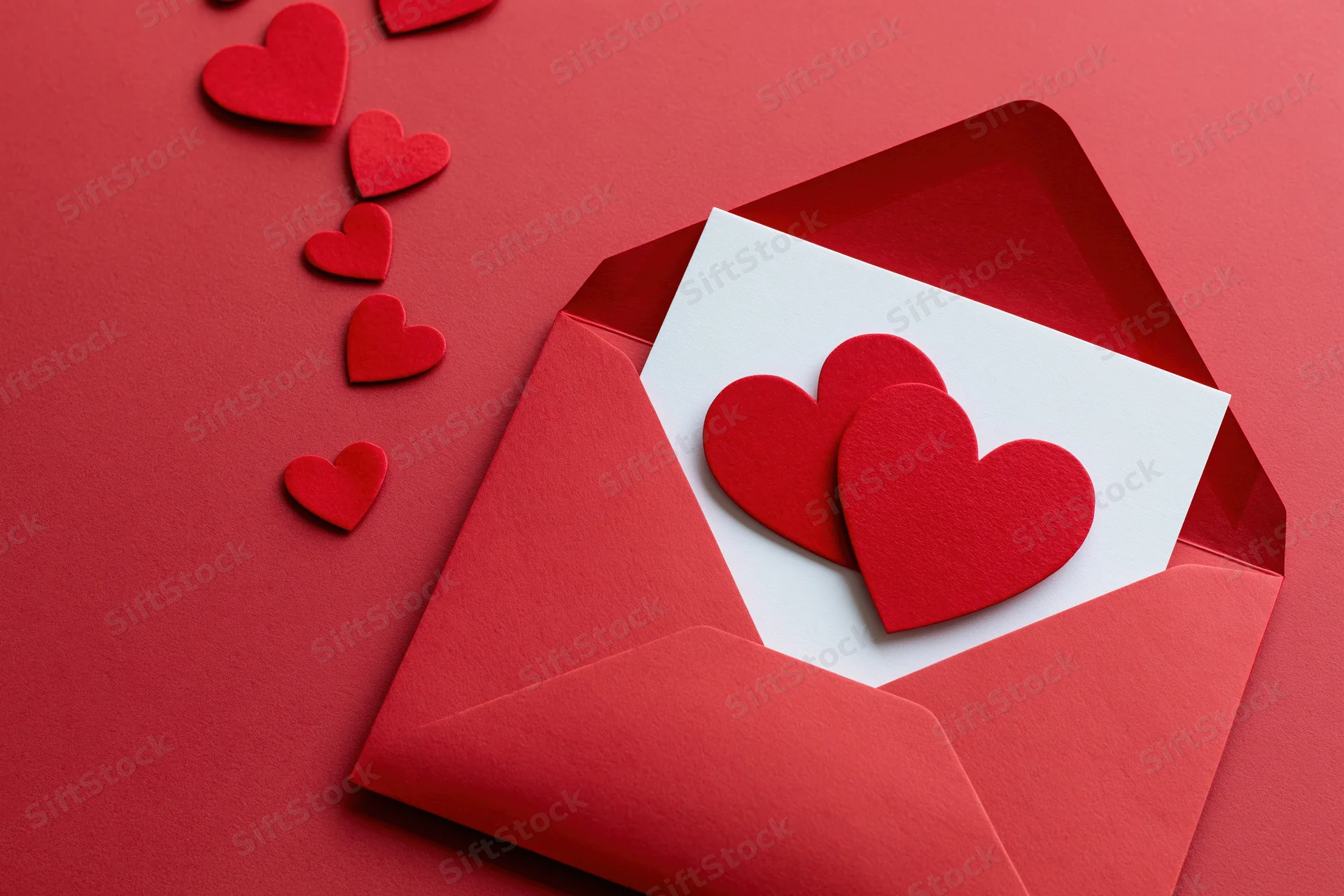 Open red envelope with heart cutouts on red background, white card inside