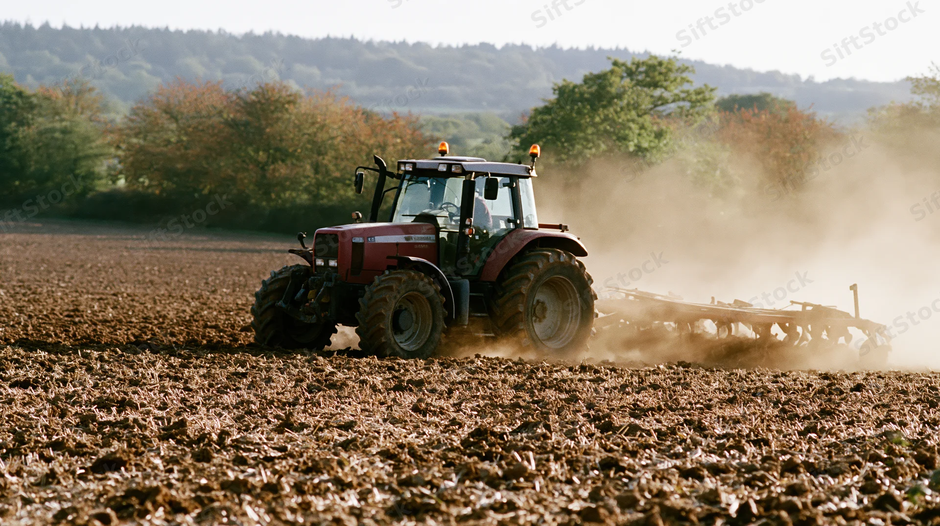 Red tractor pulling a wide harrow across a freshly plowed field