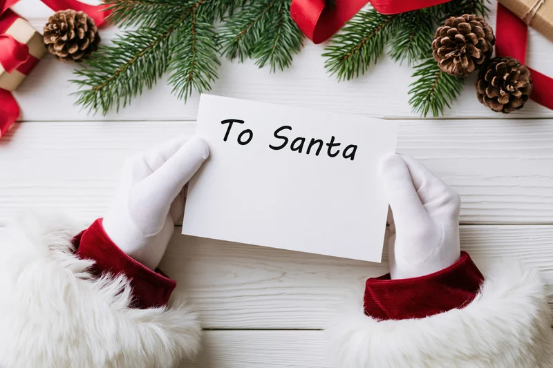 Santa's white-gloved hands holding a blank letter headed to santa on a decorated wooden surface