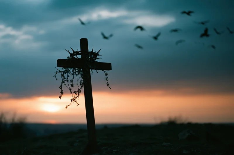 Silhouette of a wooden christian cross with a crown of thorns at sunset on a hill