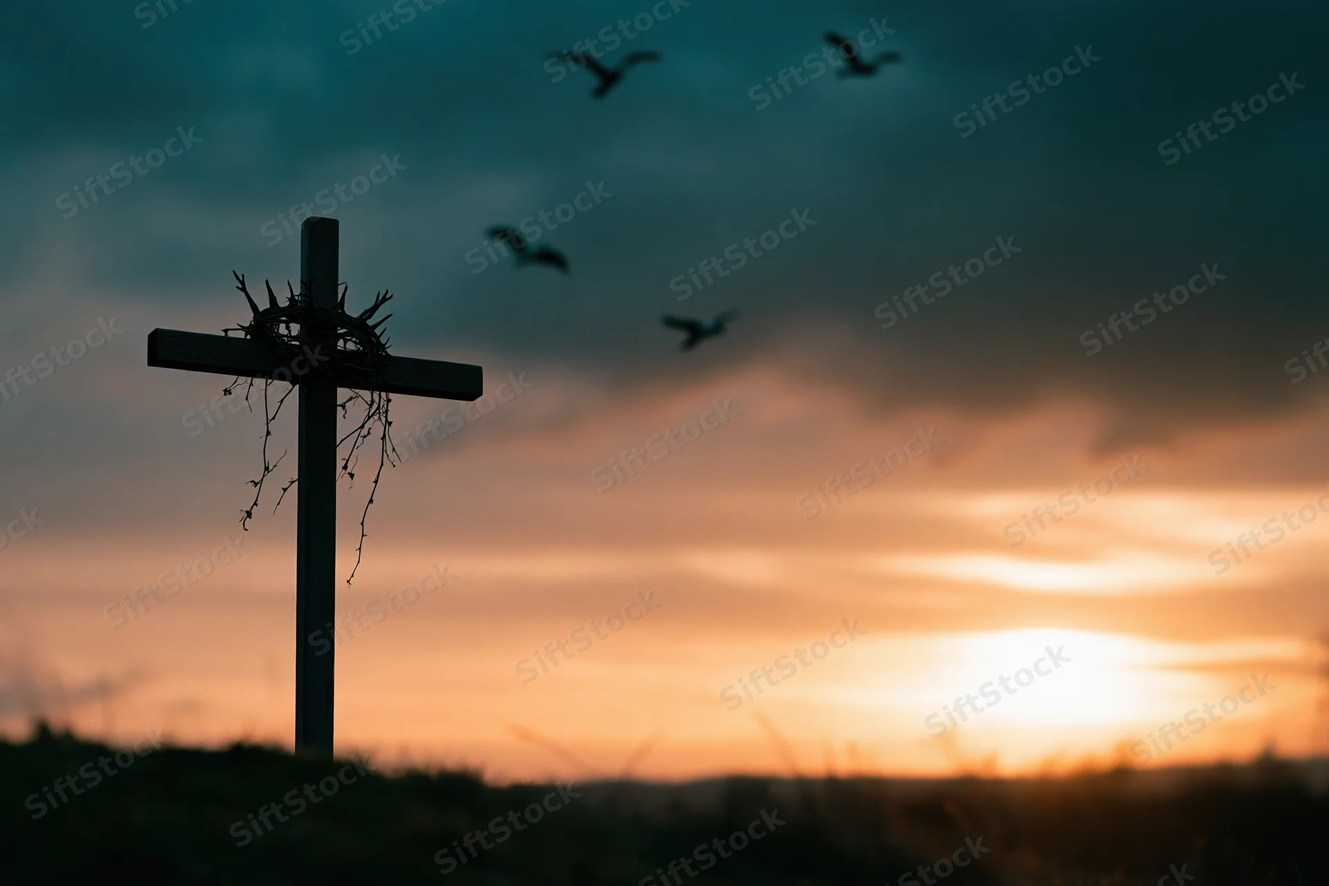 Silhouette of a christian cross with a crown of thorns against a sunset sky with birds flying overhead