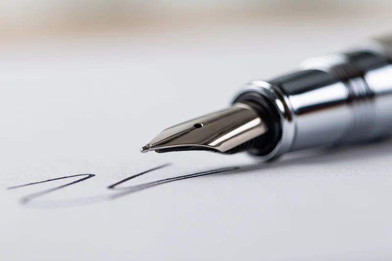Silver fountain pen nib resting on white paper with handwritten cursive script nearby