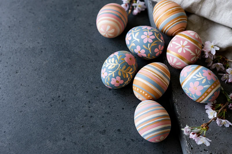 Decorated easter eggs with floral and stripe patterns arranged on a dark concrete surface with cherry blossoms