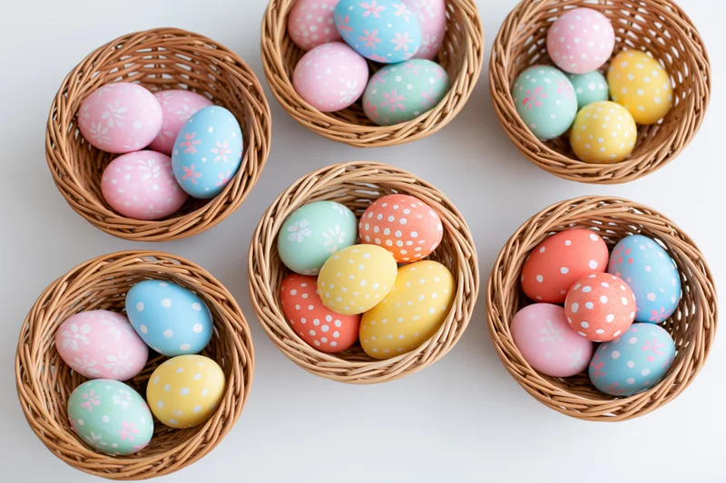 Six wicker baskets filled with pastel decorated easter eggs arranged on white surface