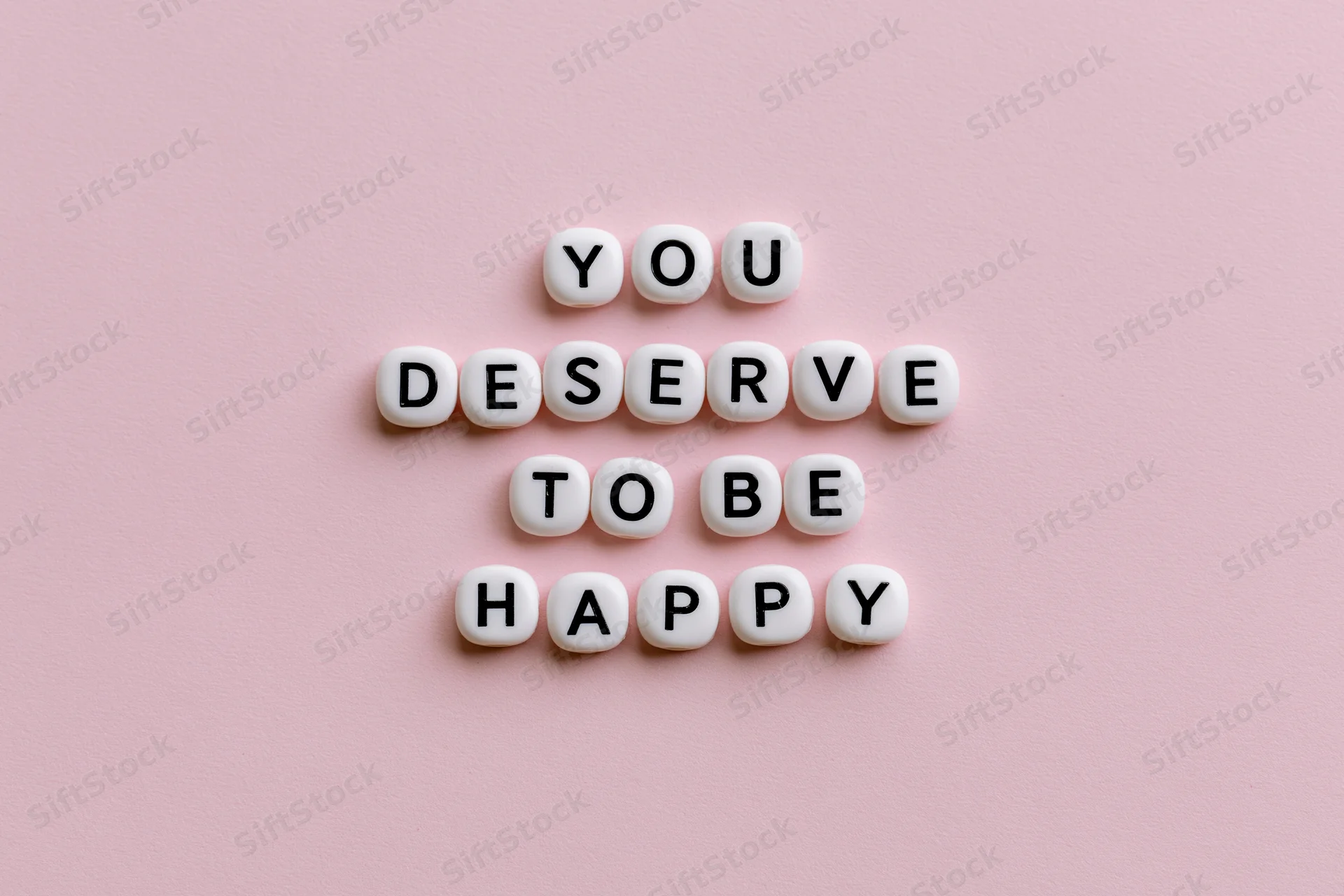 White letter beads spelling you deserve to be happy on pink background