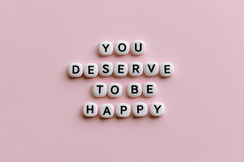 White letter beads spelling you deserve to be happy on pink background