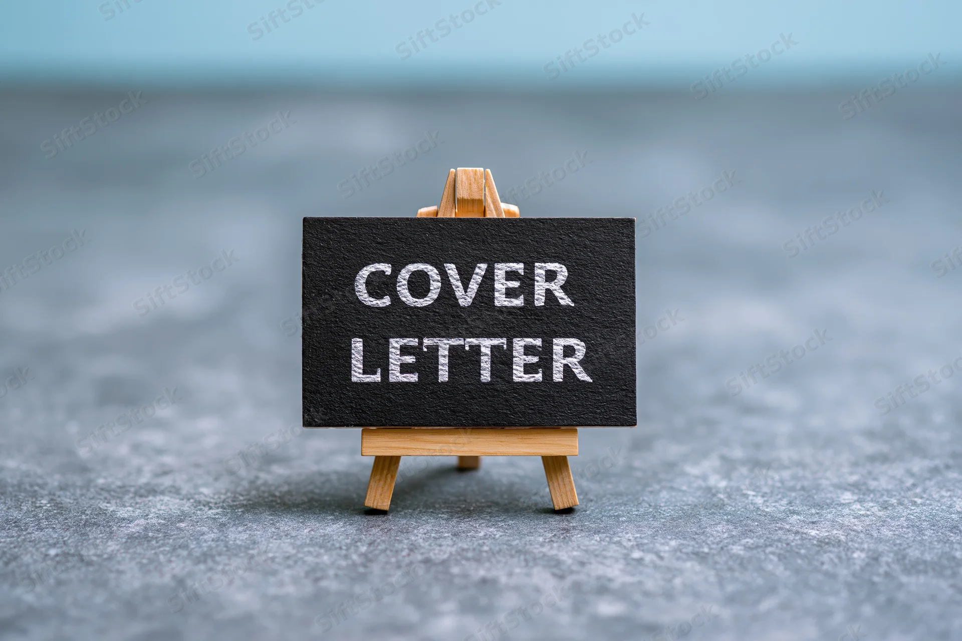 Small wooden easel holding black chalkboard sign with white text reading cover letter on gray surface