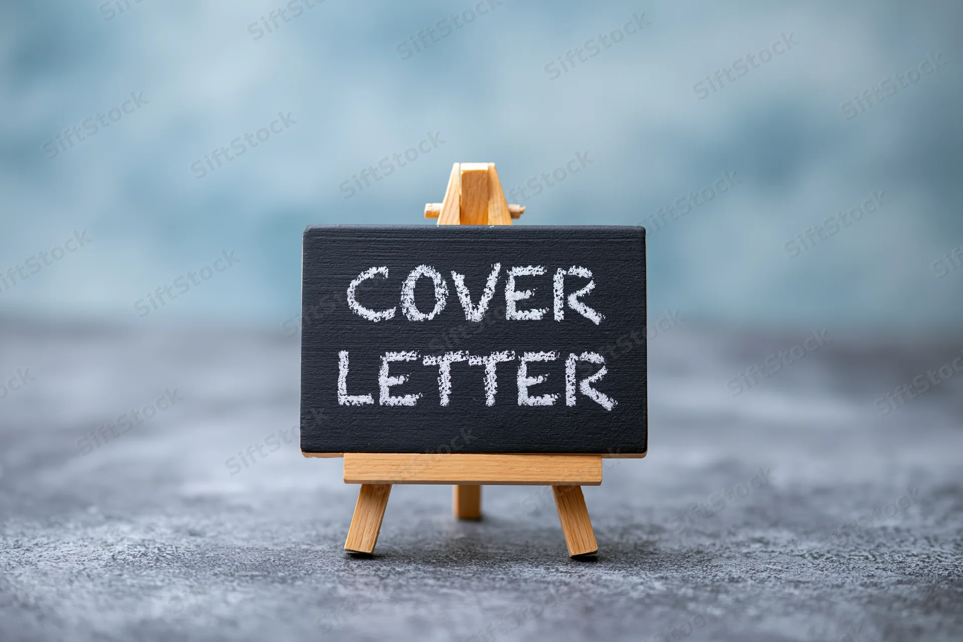 Small wooden easel holding black chalkboard with white chalk text reading cover letter on textured gray surface