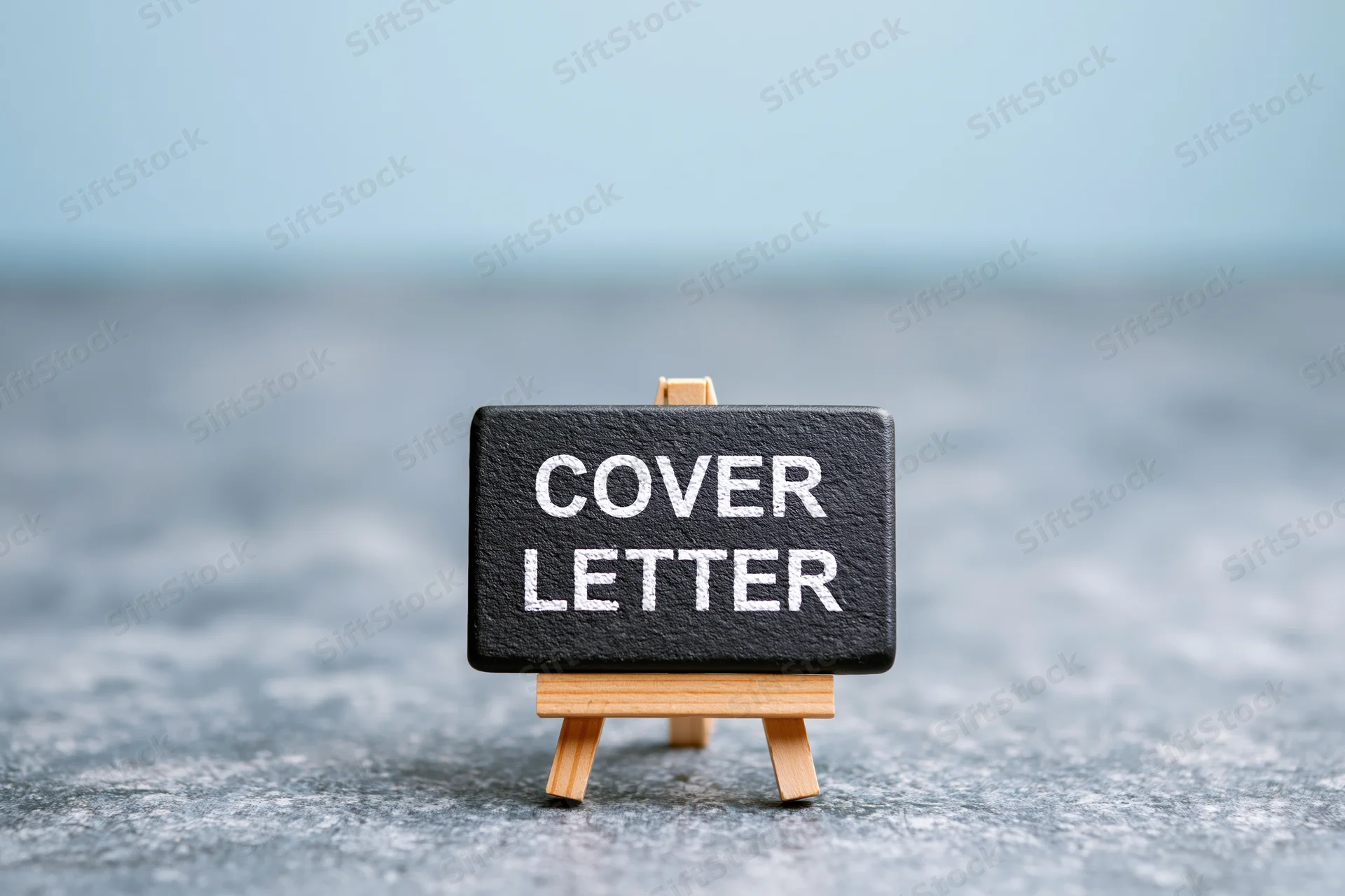 Small wooden easel holding black chalkboard sign with white text reading cover letter on gray surface
