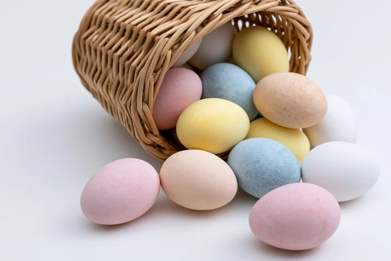 Pastel-dyed eggs spilling from a tipped wicker basket on white surface