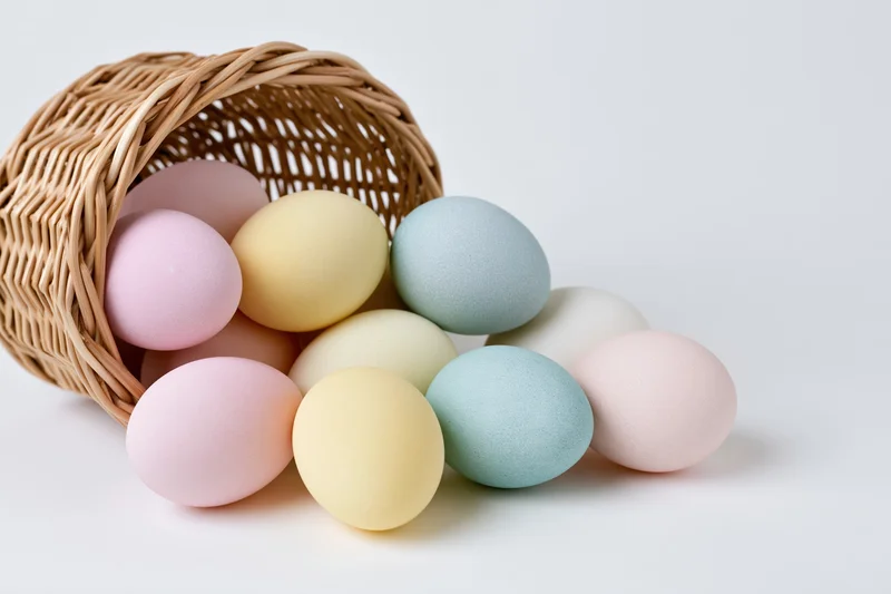 Pastel-dyed eggs scattered from a tipped wicker basket on white surface
