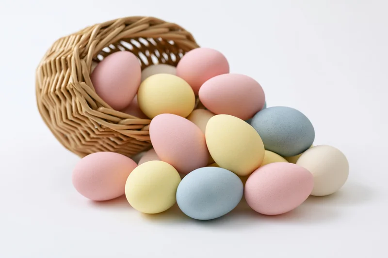 Pastel-dyed eggs spilling from a tipped wicker basket on white background