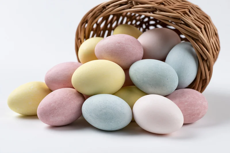 Pastel-dyed eggs spilling from a tipped wicker basket on white background