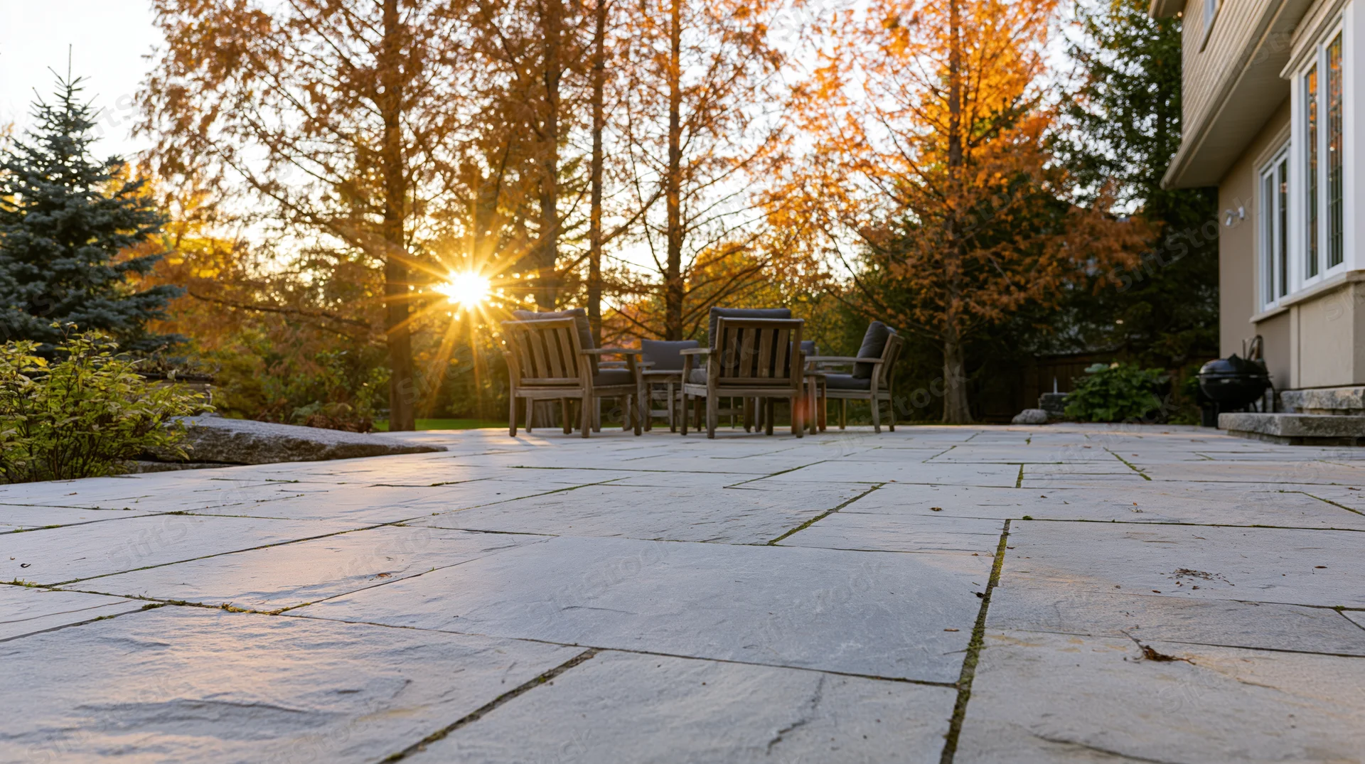 Stone patio in suburban backyard at golden hour with autumn trees and outdoor furniture