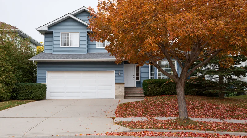 Blue-grey suburban house with white garage and autumn tree in front yard