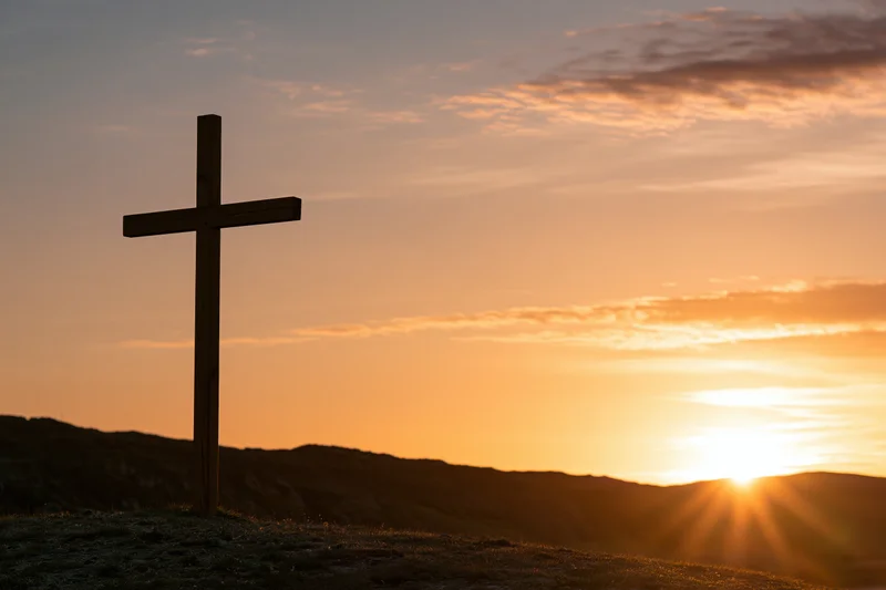 Wooden christian cross silhouetted on a hilltop at sunset