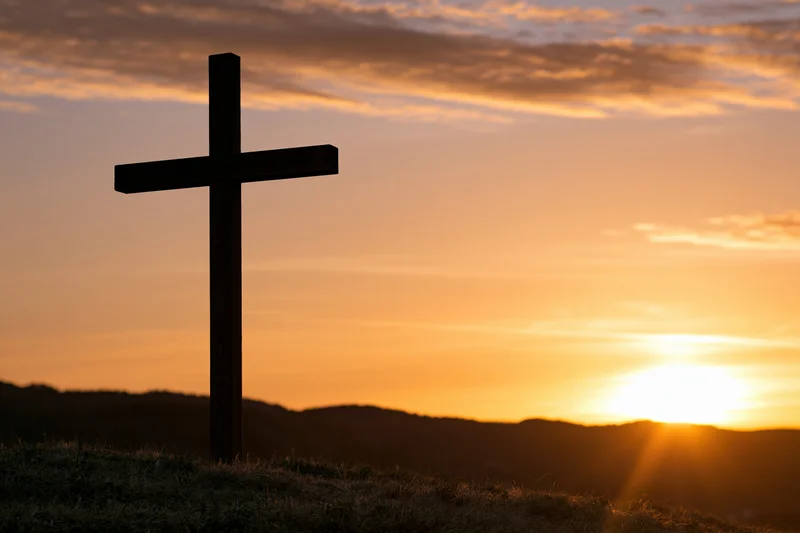 Wooden christian cross silhouetted on a hilltop at sunset