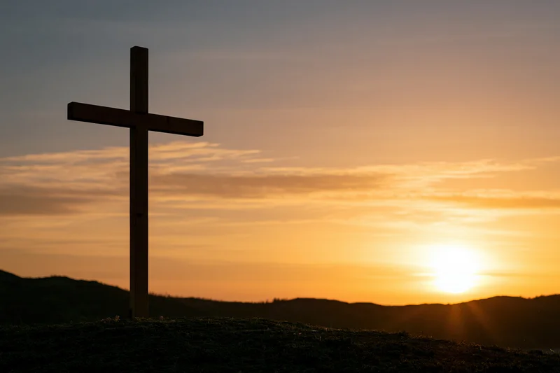 Wooden christian cross silhouetted on a hilltop at sunset
