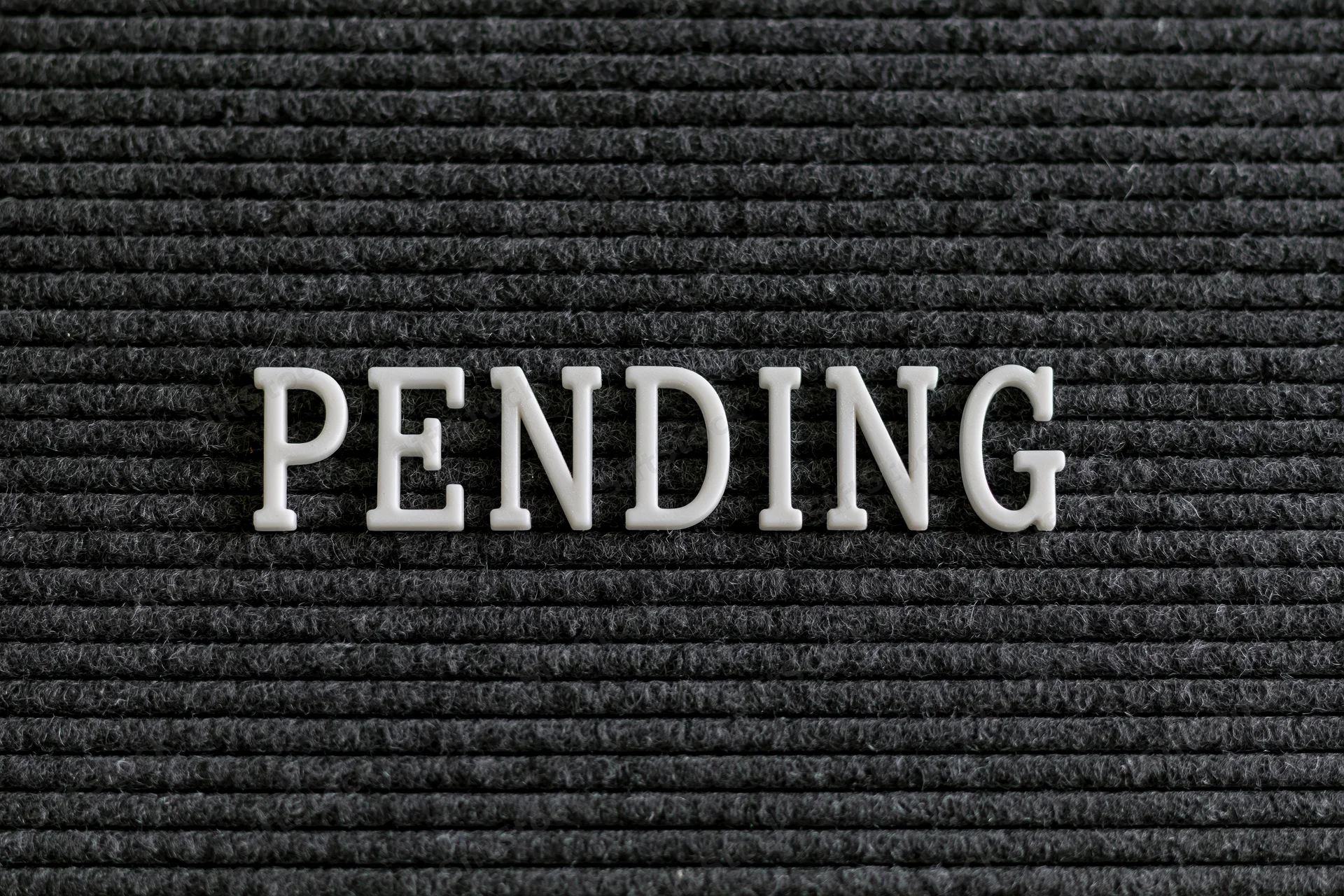 White plastic letters spelling pending on a black ribbed fabric surface