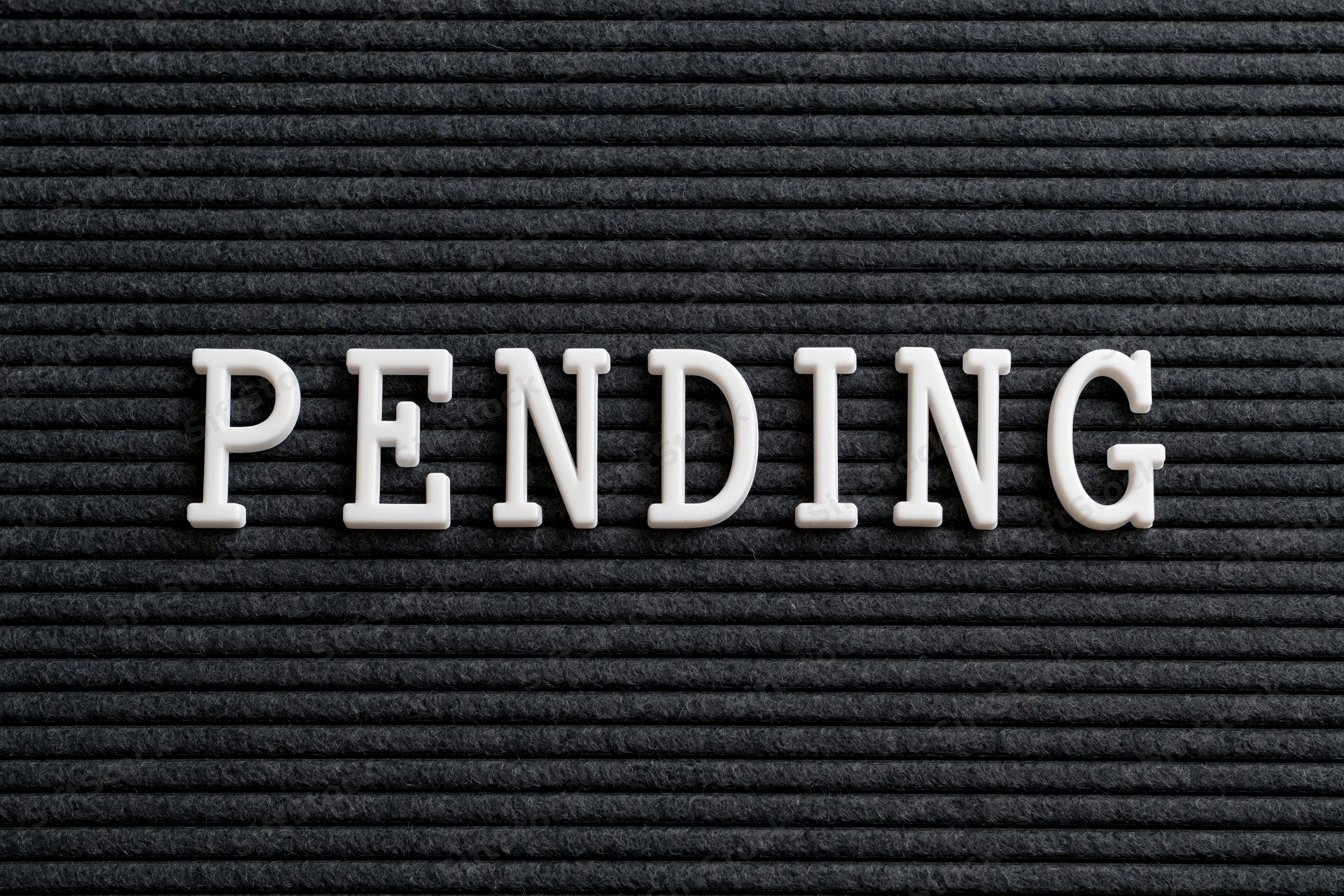 The word pending spelled in white plastic letters on a black textured board