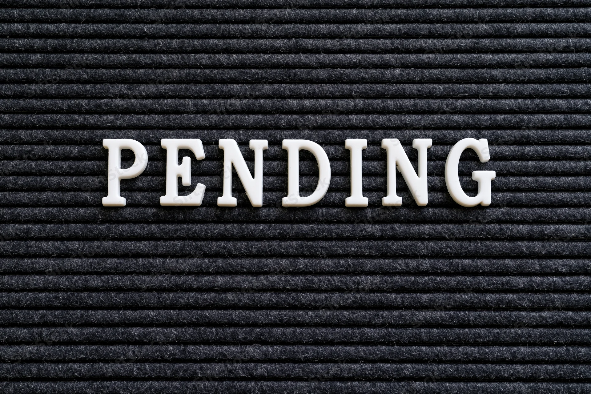 White plastic letters spelling pending on a black ribbed surface