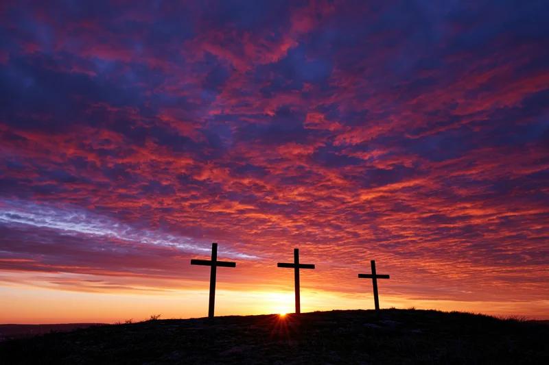 Three christian crosses silhouetted on a hilltop at sunset
