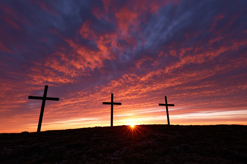 Three christian crosses silhouetted on a hilltop at sunset