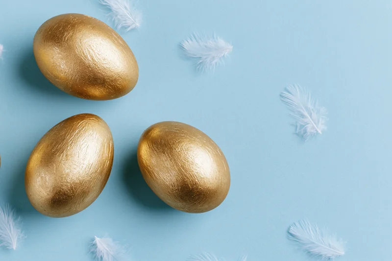 Golden painted easter eggs with white feathers on blue background