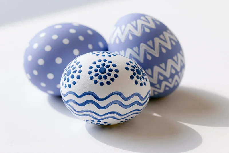 Three hand-painted easter eggs with blue and white patterns arranged in a loose triangular formation on a white surface