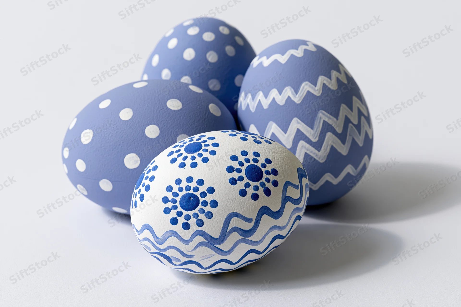 Four hand-painted easter eggs with blue and white patterns arranged in a loose triangular formation on a white surface