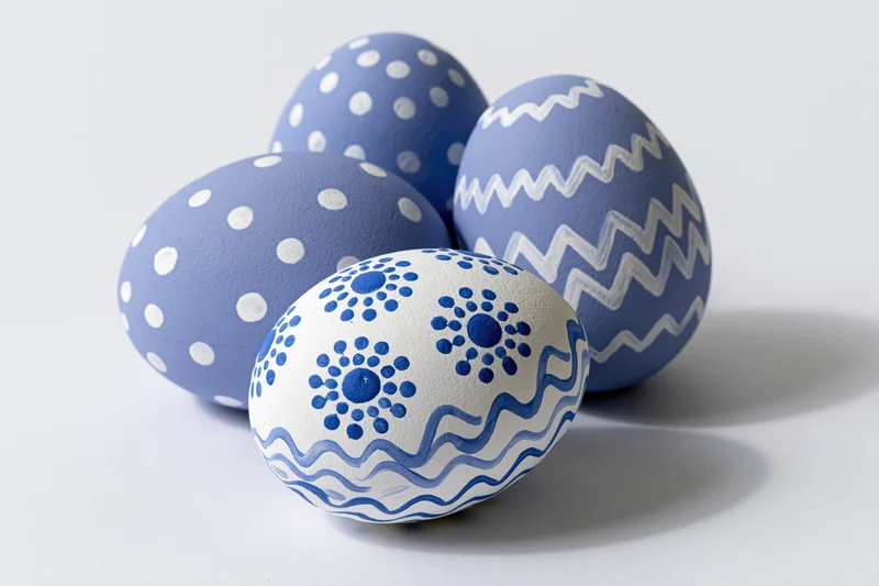 Four hand-painted easter eggs with blue and white patterns arranged in a loose triangular formation on a white surface