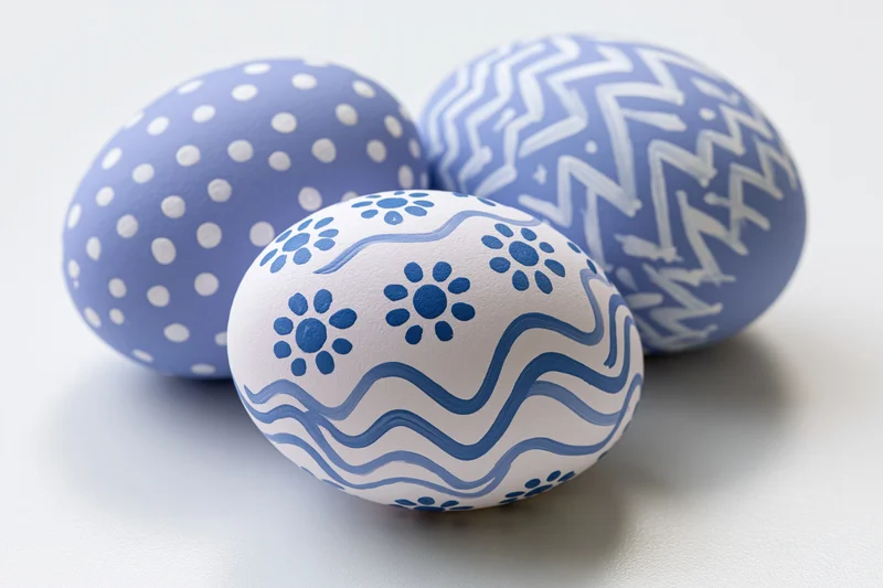 Three hand-painted easter eggs with blue and white patterns arranged in a loose triangle on a white surface