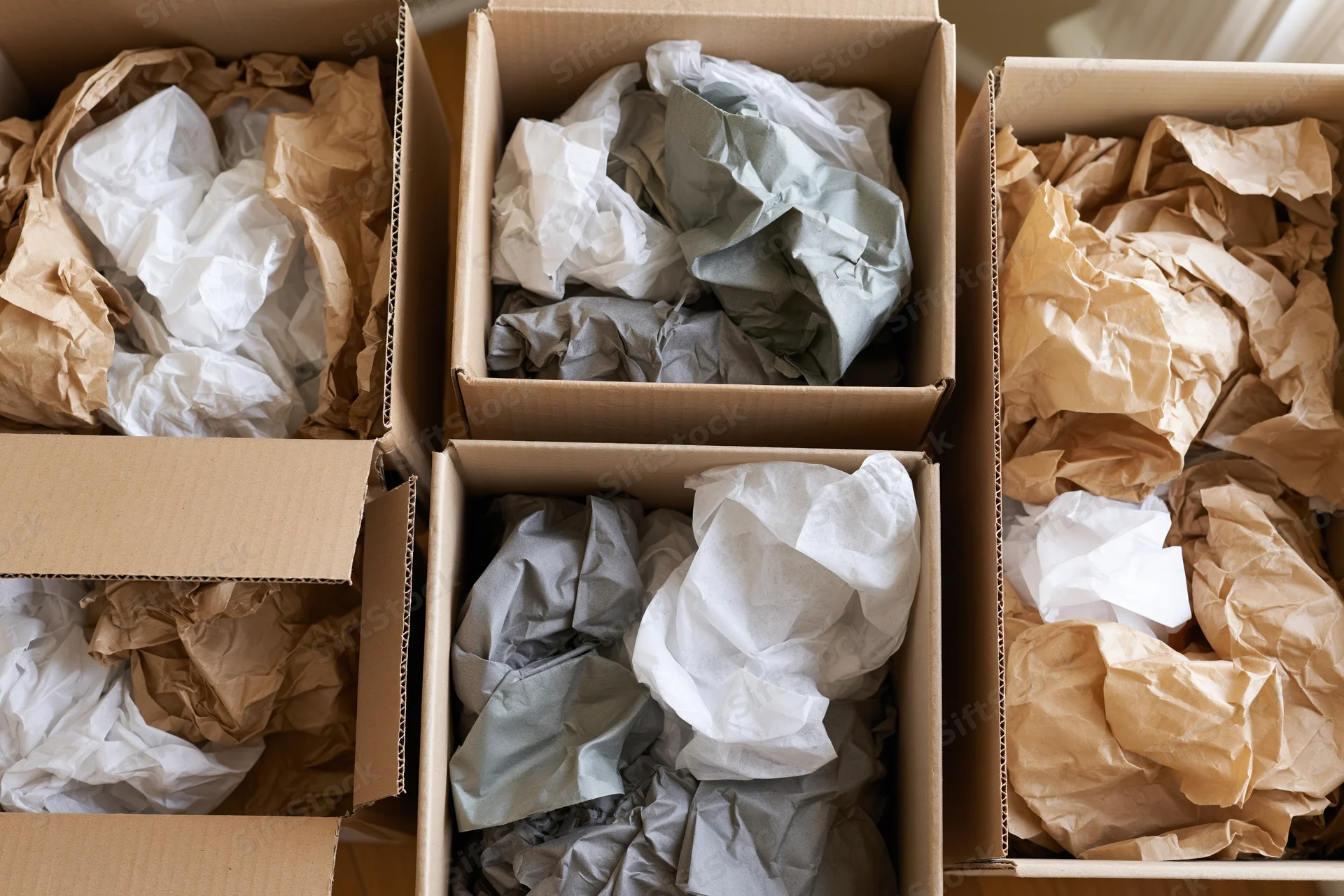 Open cardboard shipping boxes filled with crumpled kraft and tissue paper for protective packaging